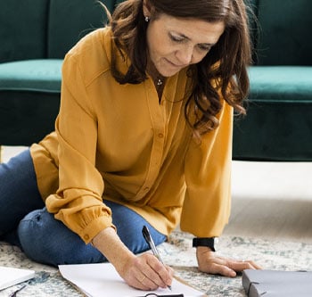 Woman in yellow shirt sitting on the floor and taking notes