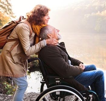 Woman leaning over man in wheelchair while they stare at nature